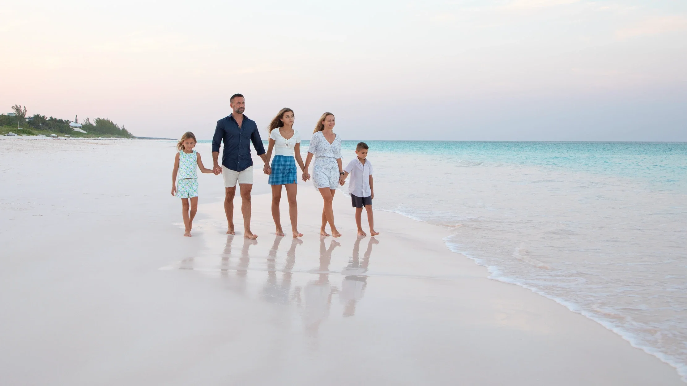 The Lockwood family walking hand in hand along a pink-sand beach at dusk