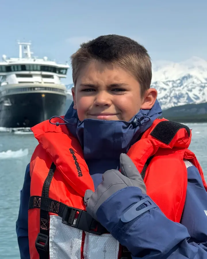 Colt Lockwood in a life vest on a Zodiac, an expedition ship behind him