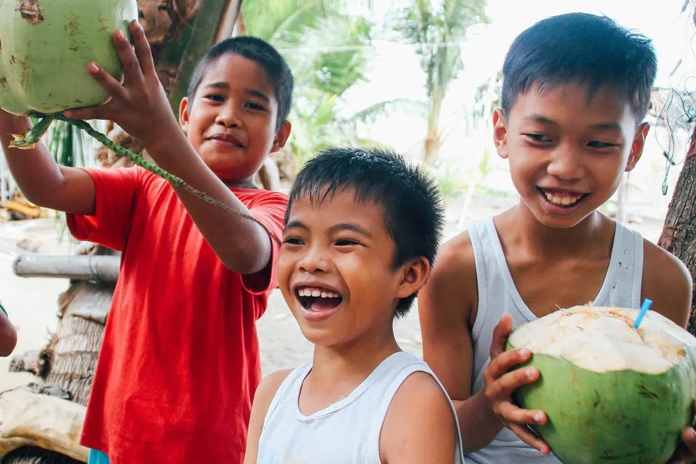 Three boys laughing and holding green coconuts