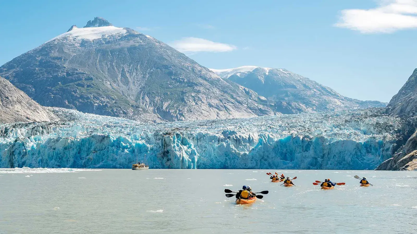 Kayakers paddle in front of a glacier