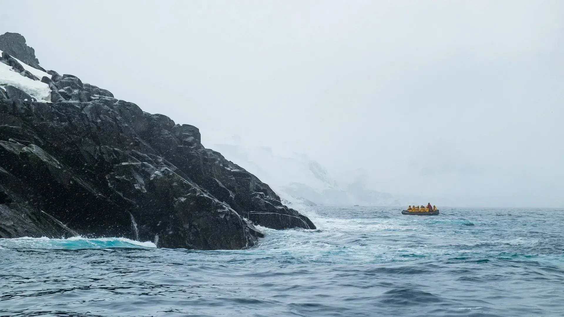A lone Zodiac boat cruises past a rocky shore in Antarctica