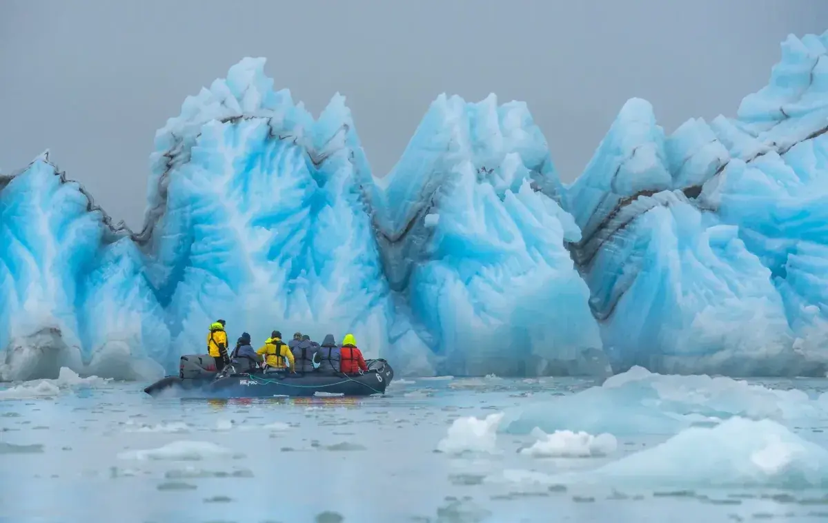 Antarctic explorers ride a zodiac along ice structures