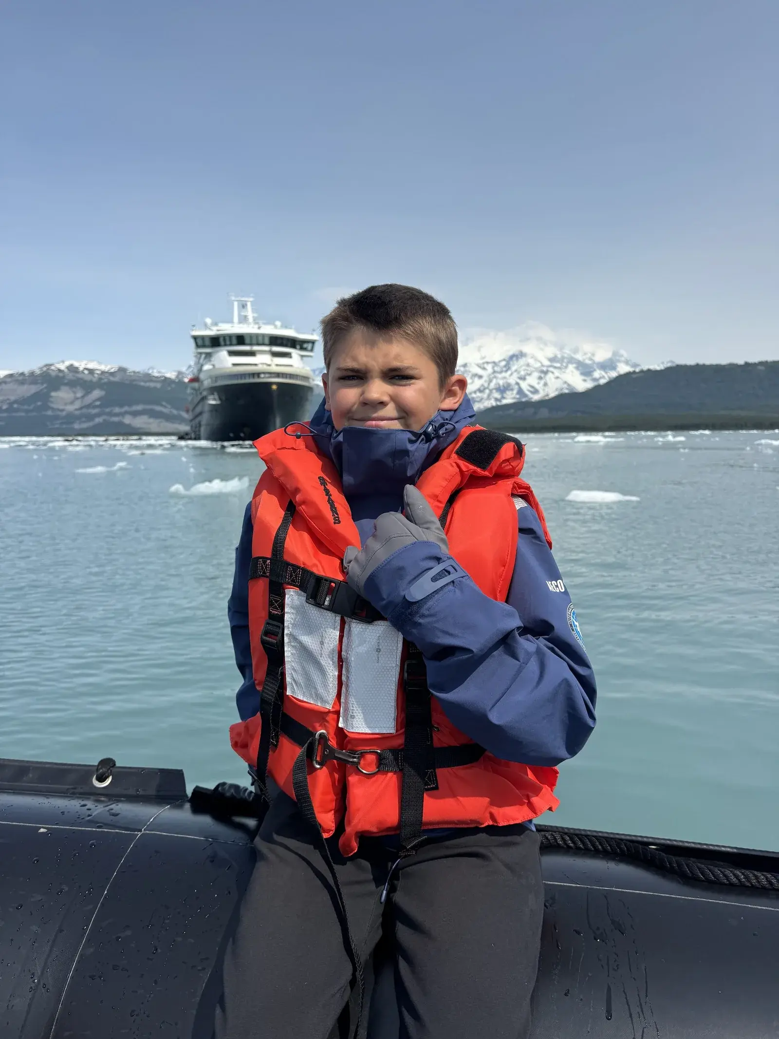 Colt on a Zodiac in Icy Bay, Alaska, an expedition ship and snow peaks behind him