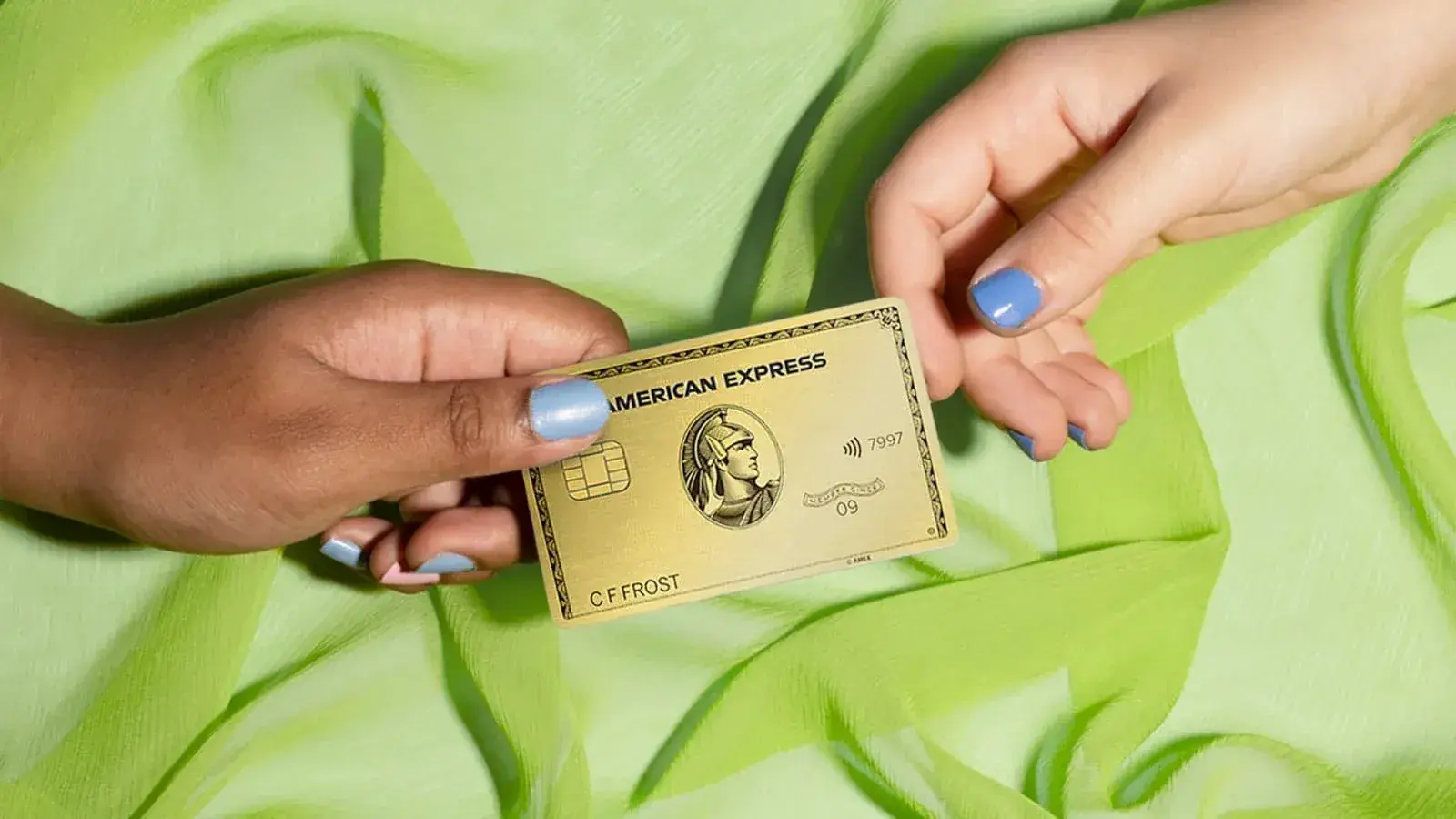 One person's hand passes an American Express Gold Card to another person's hand