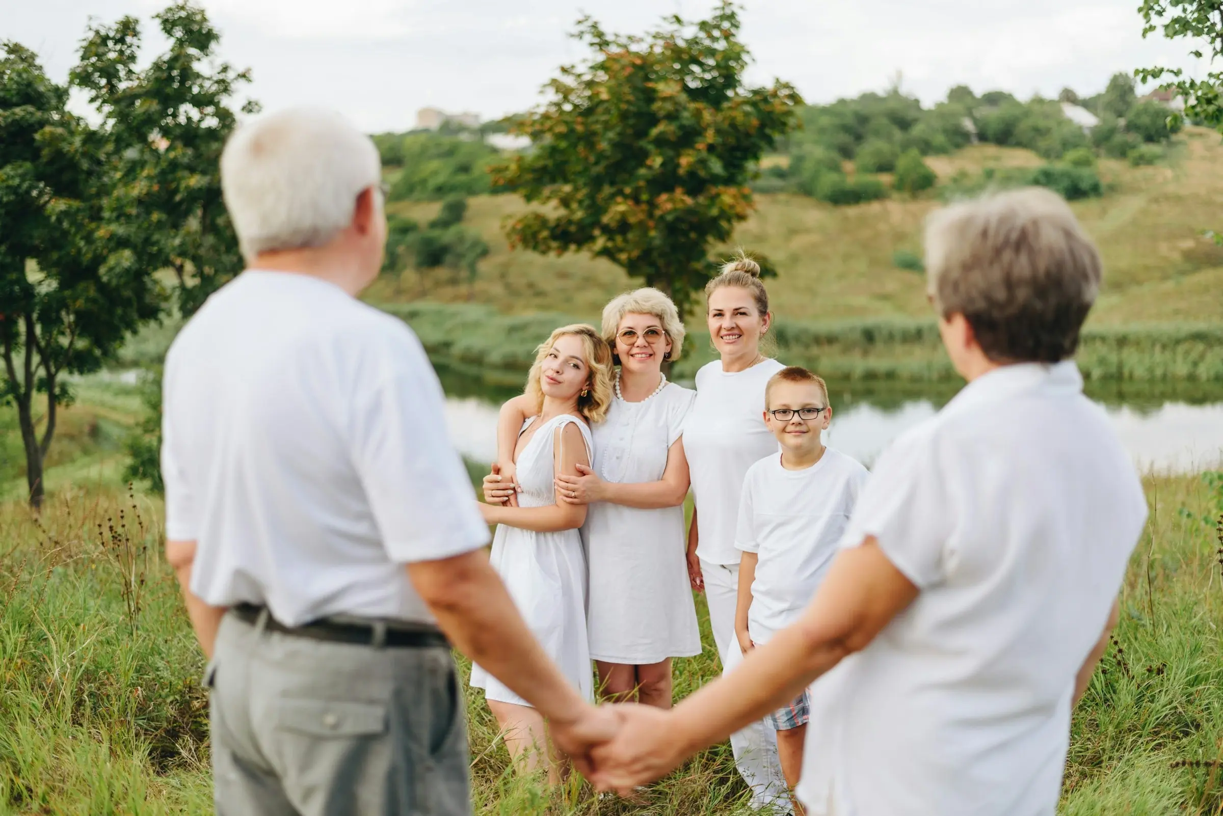 Grandparents holding hands in the foreground while their daughter and grandchildren smile from a summer field