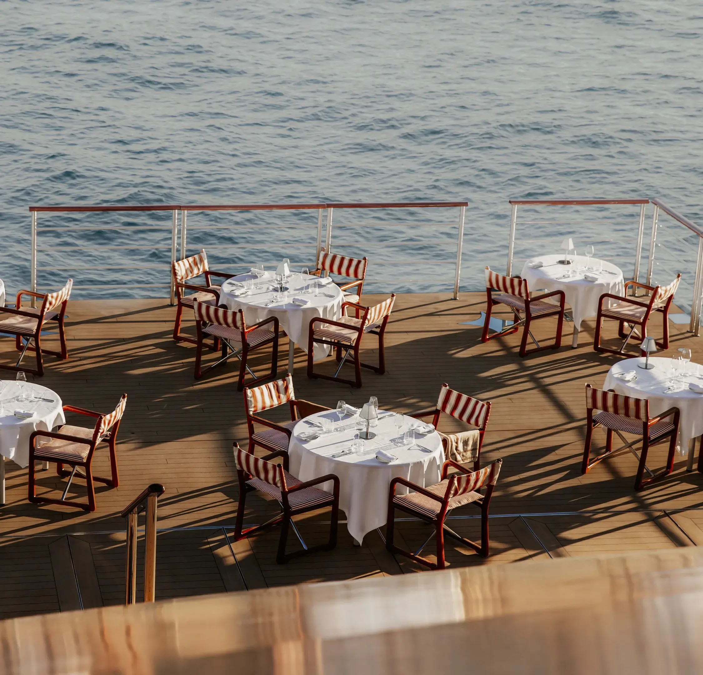 Tables set with white linen on the open-air dining deck of Orient Express Corinthian