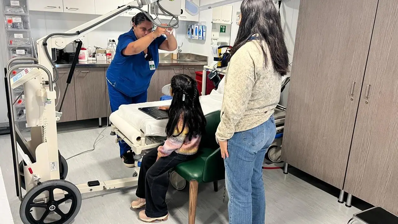 A Seabourn Pursuit crew member positions an X-ray machine over a young girl's hand in the ship's medical center while her mother looks on