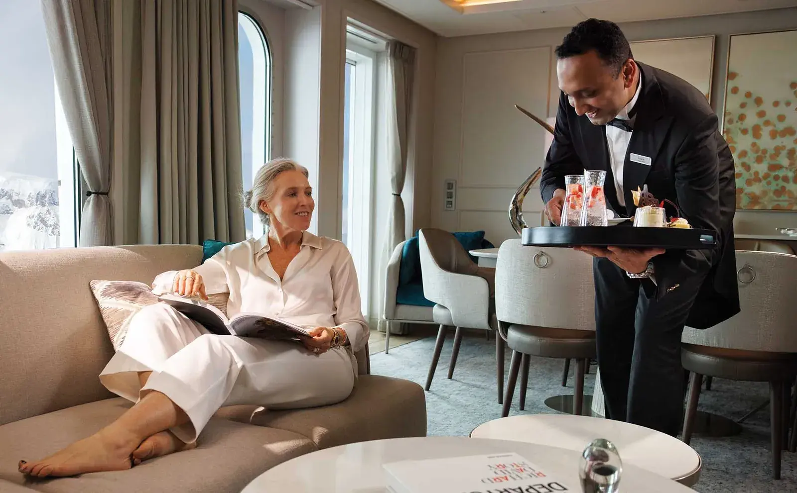 A butler in a tux serves a Silversea guest in her cruise cabin