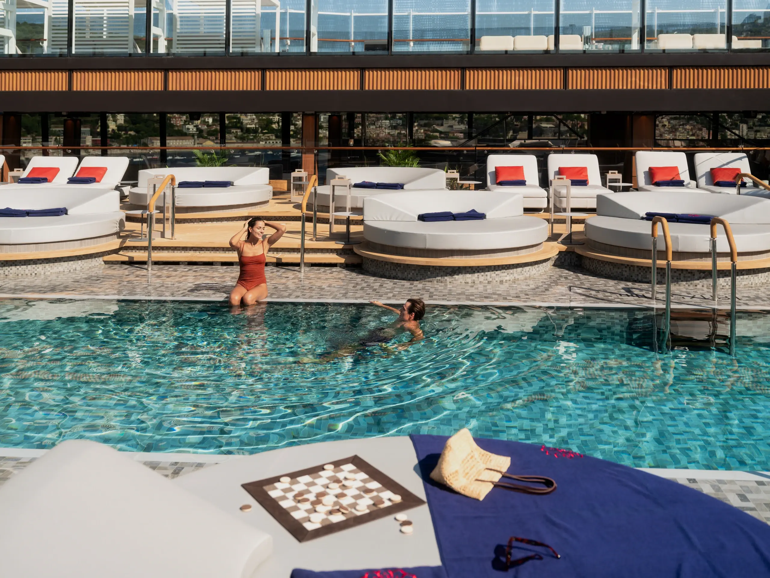 Guests swim in the Conservatory Pool aboard Explora III, ringed by white daybeds