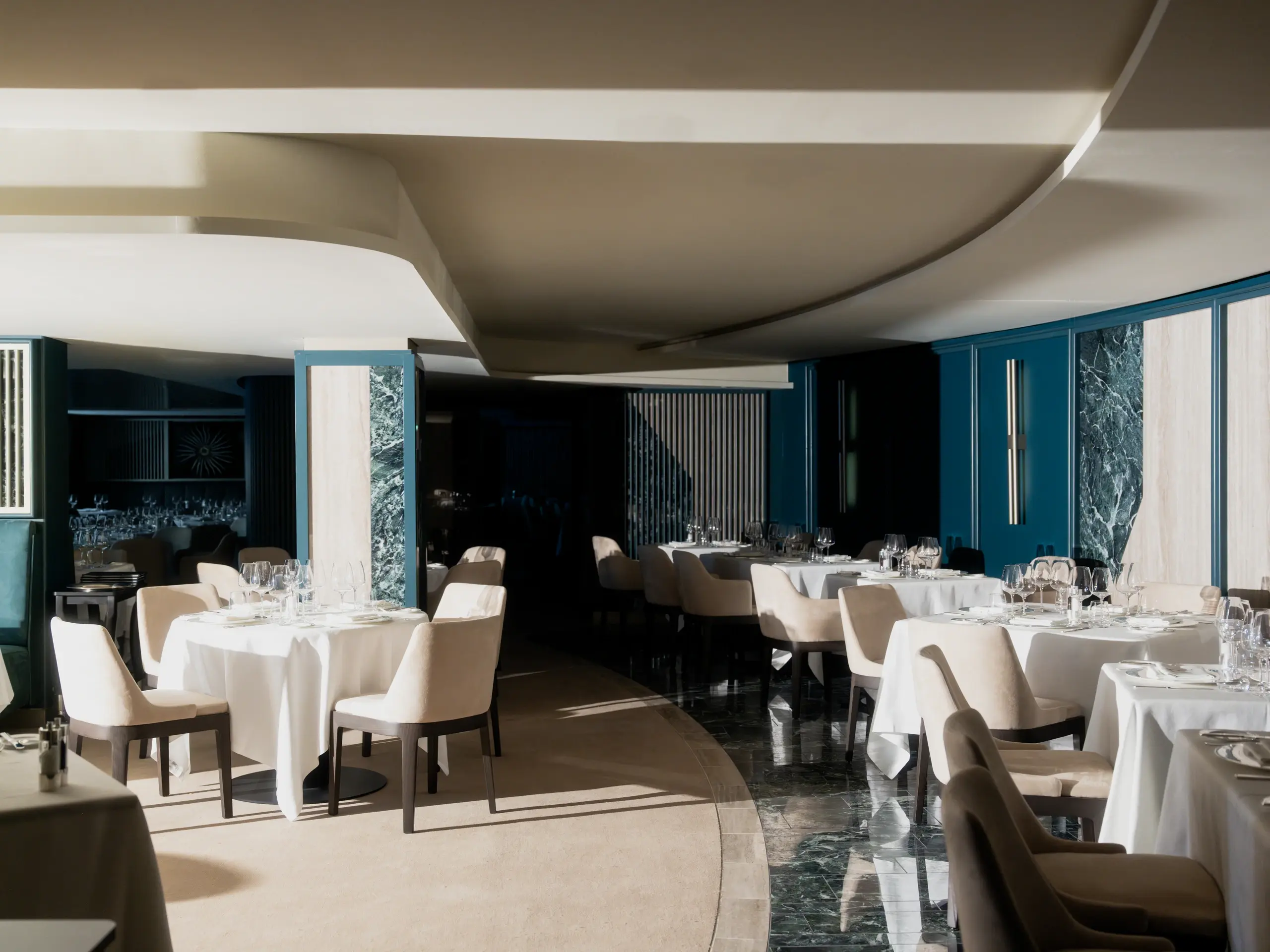 Fil Rouge restaurant aboard Explora III, with white-clothed tables, green marble pillars and teal walls