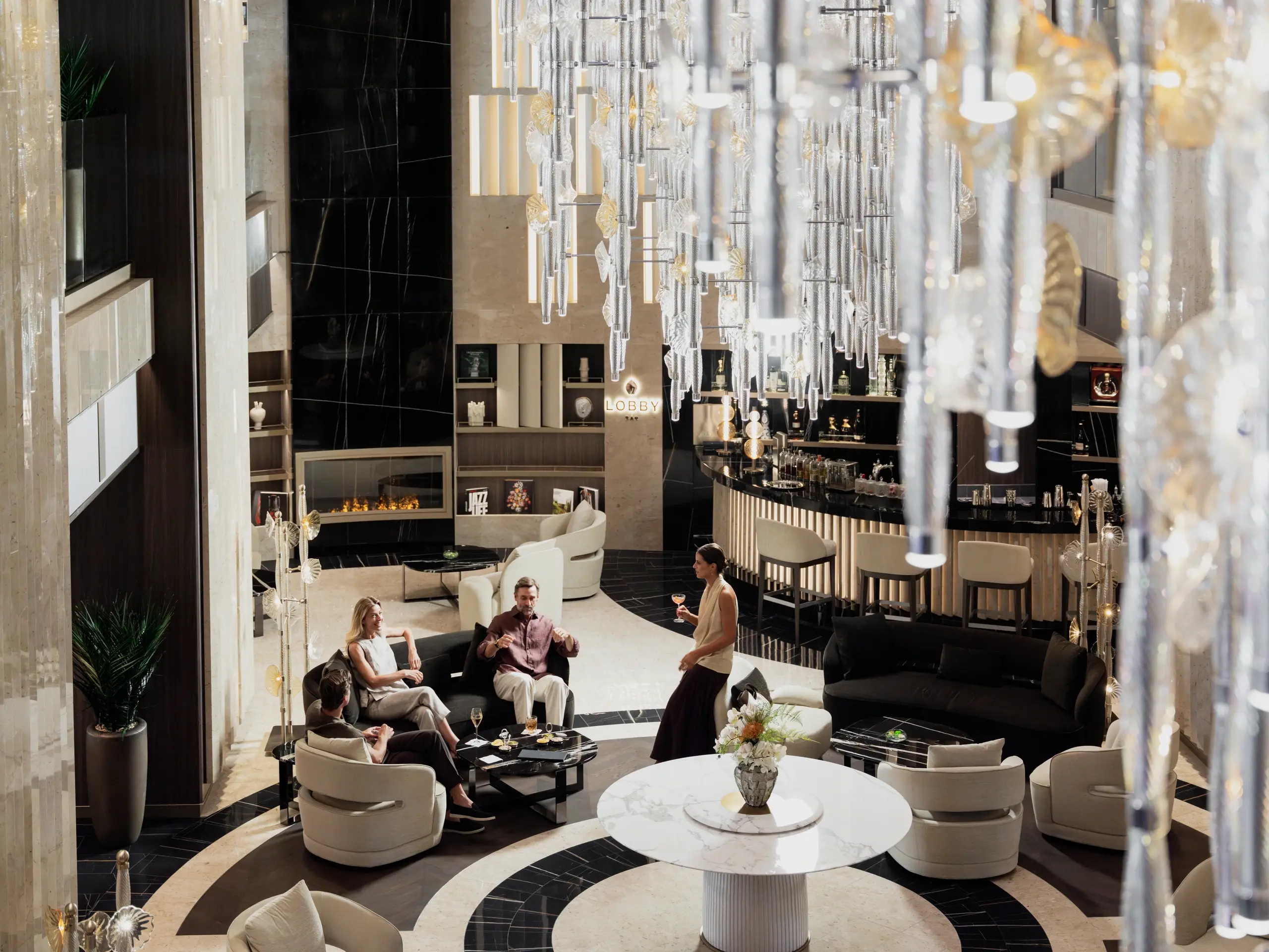 Guests with drinks in the Explora III lobby lounge beneath a cascading glass chandelier