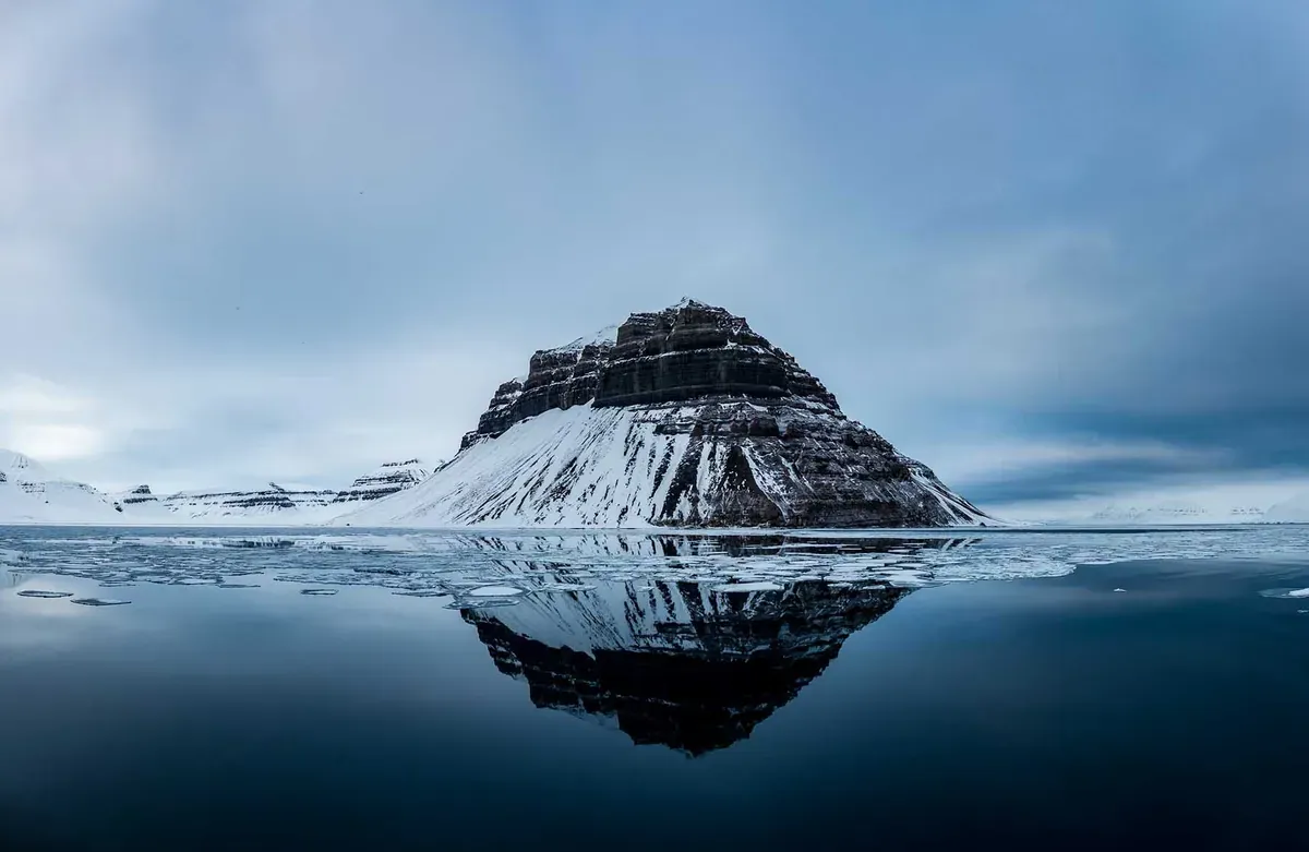 A small, snowy mountain in the middle of water in Svalbard