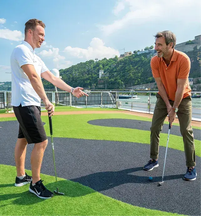 Two men play mini golf on the deck of a river cruise ship