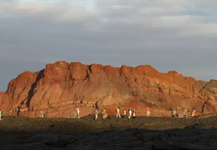People walk in front of a sun-drenched mountain cliff