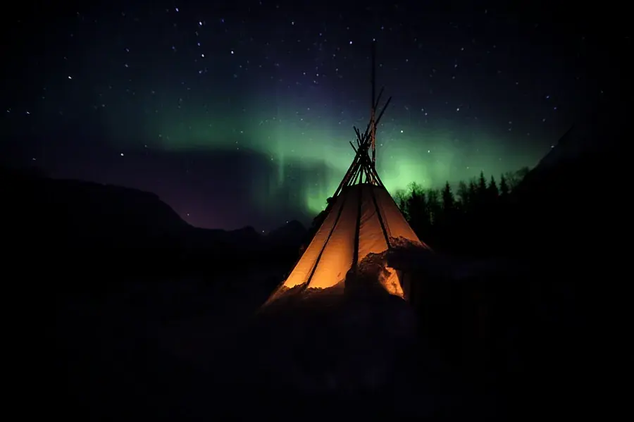 Glowing teepee camp lit from within on an Arctic Norway beach at dusk