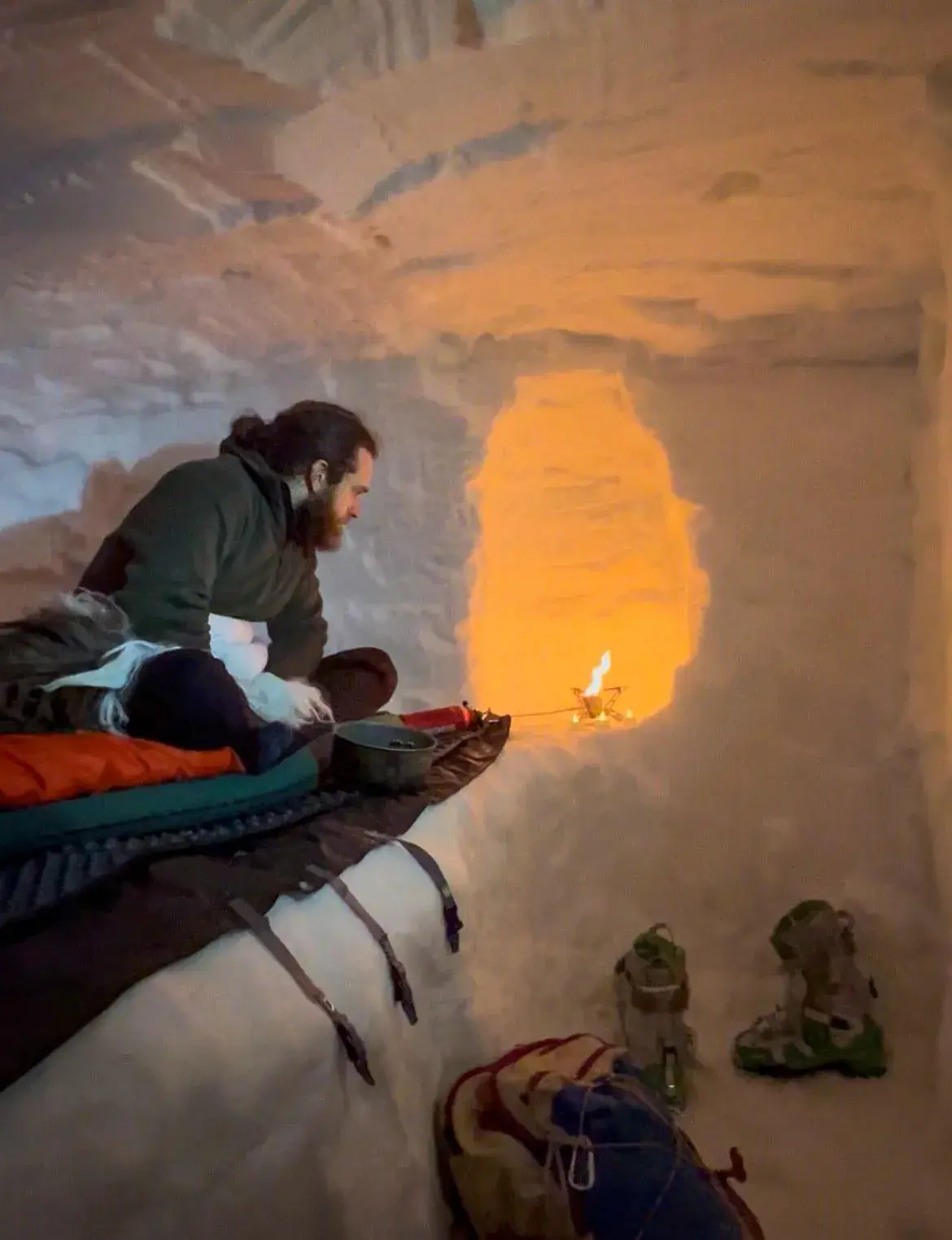Man sits on a sleeping bag in a snow cave