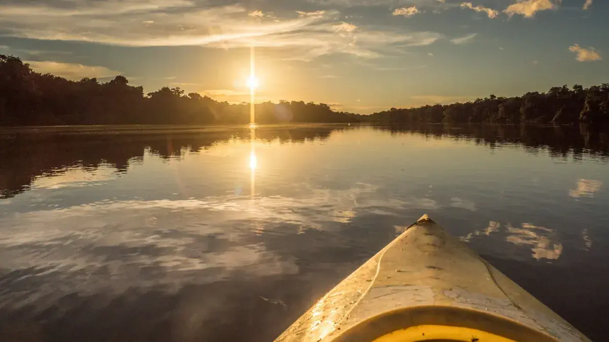A canoe travels toward a sunset on the Amazon River