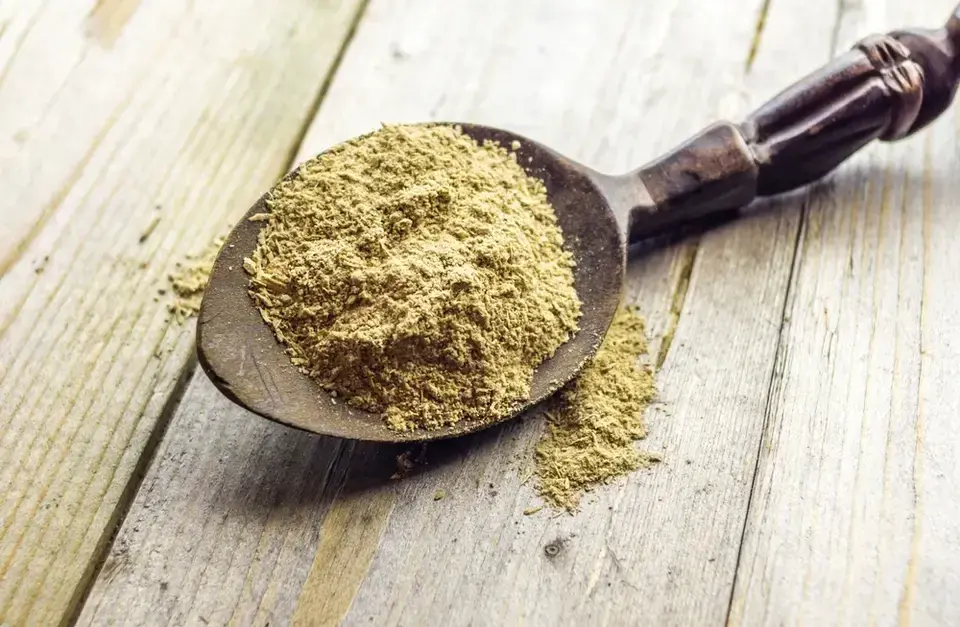 A wooden spoon full of a spice on a wooden table