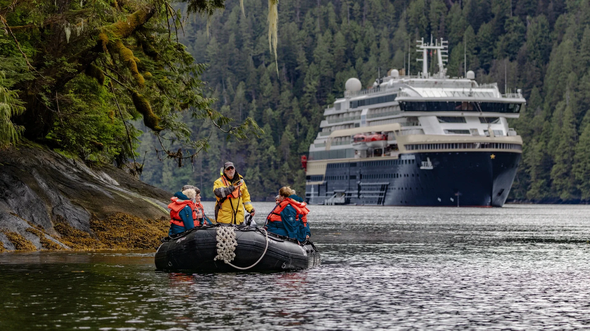 Guests on a Zodiac in a misty Alaskan fjord, an HX expedition ship anchored behind
