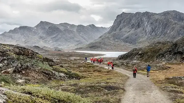 Hikers walk on a trail in Greenland with mountains in the background