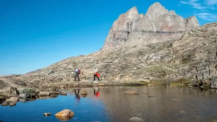 Hikers walk past a mountain peak in Greenland