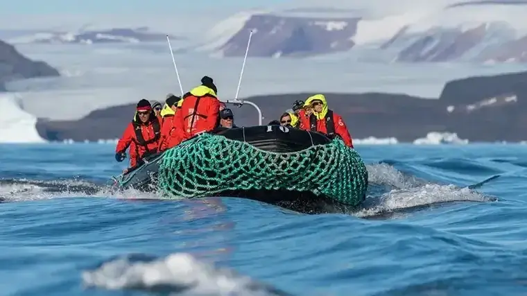 A zodiac with several explorers cruises through icy Greenland waters