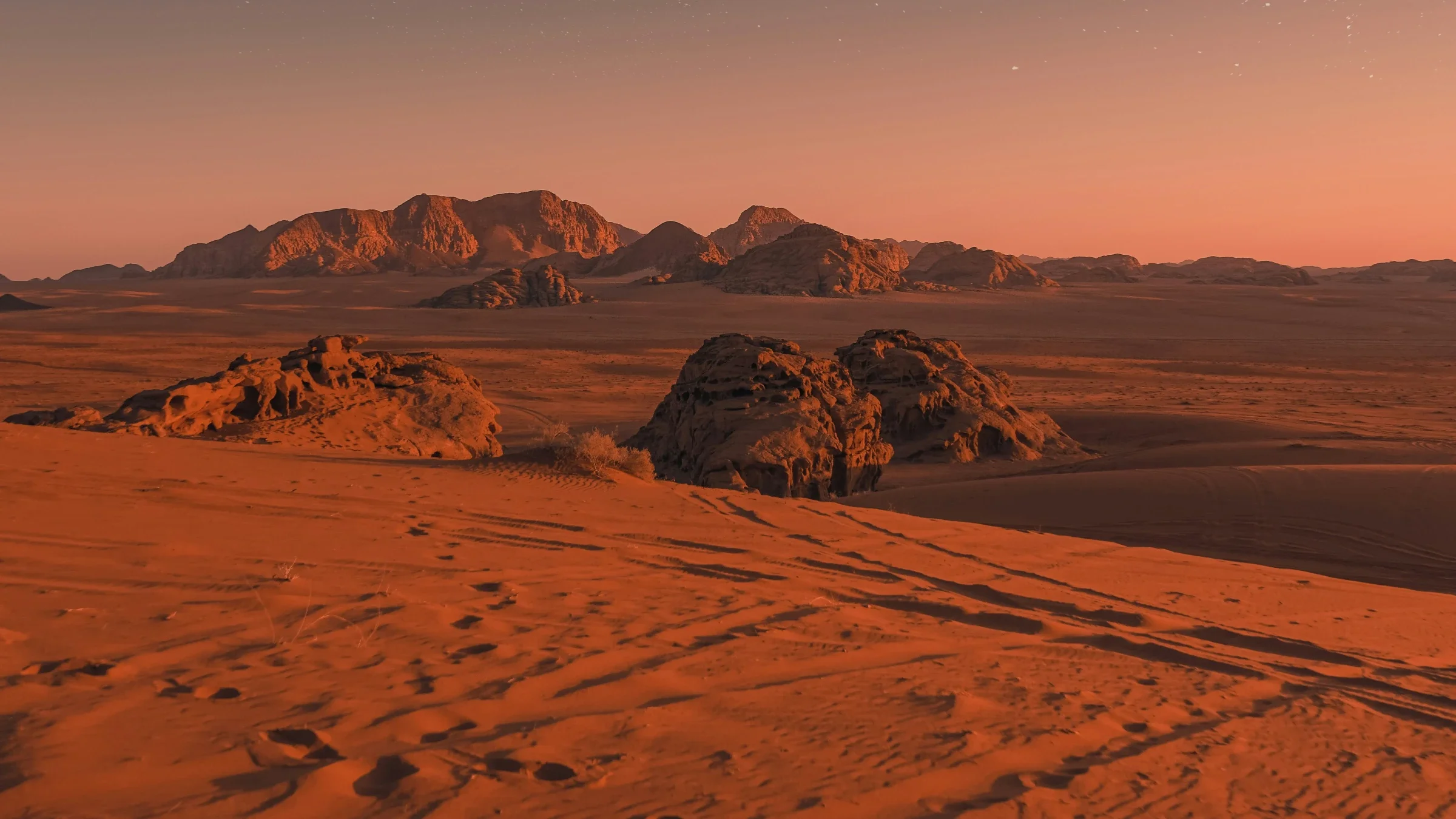 The red sandstone desert of Wadi Rum at dusk beneath a darkening, star-flecked sky
