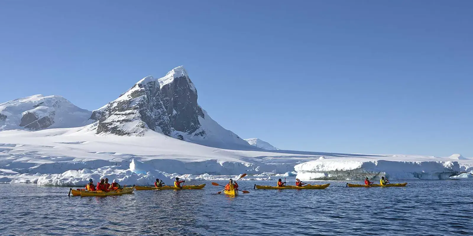 Kayakers paddling past towering icebergs and snow-capped mountains in Antarctica