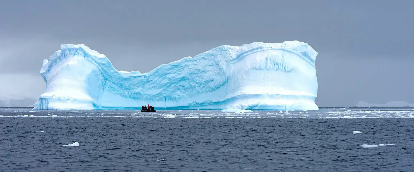 Zodiac expedition boat cruising past a massive iceberg in Antarctica