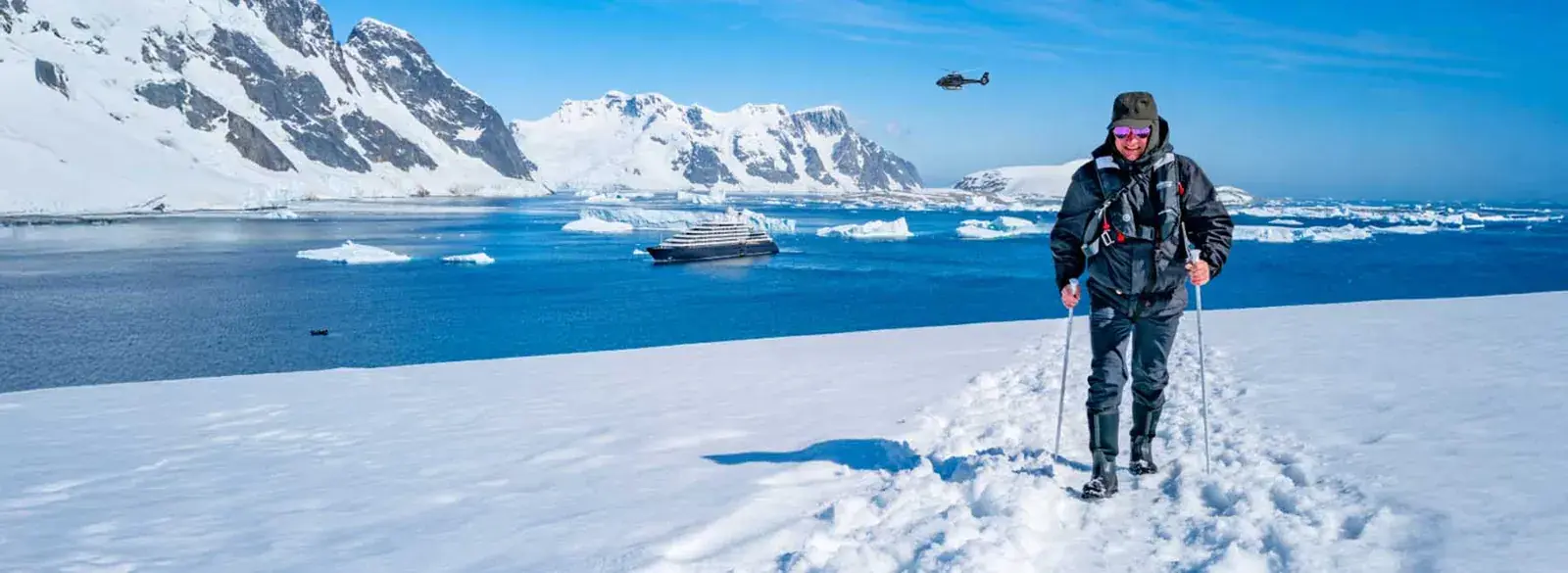 A hiker on an Antarctica hilltop overlooking Scenic Eclipse in the harbor below