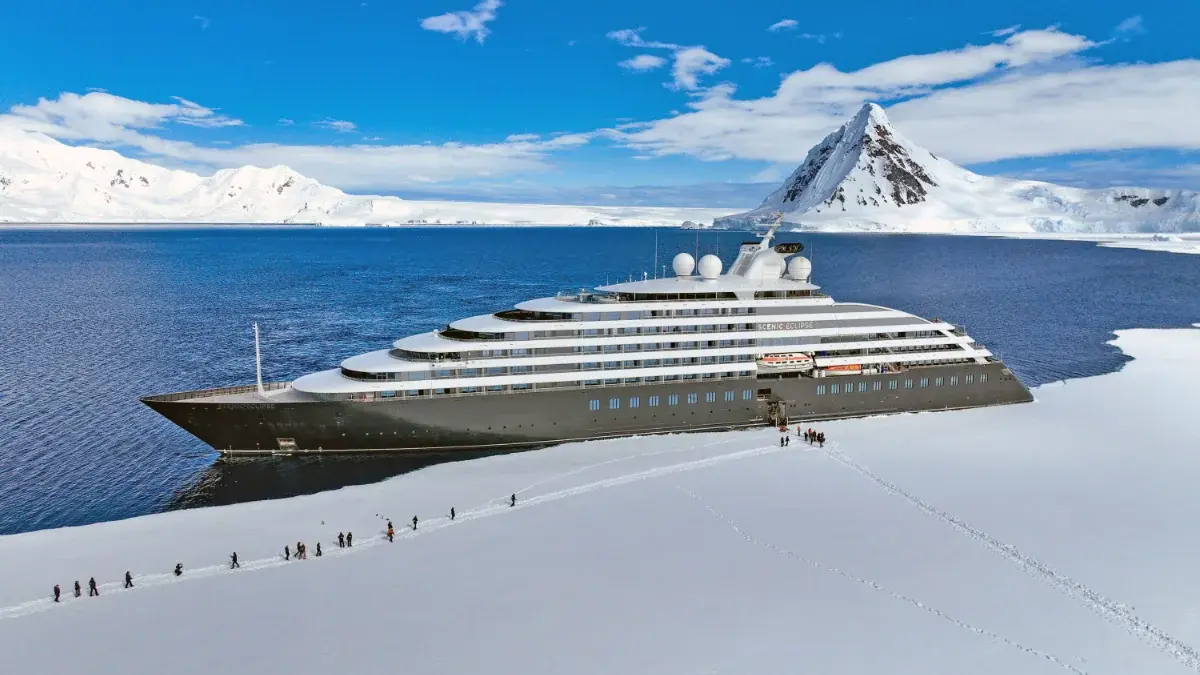 Scenic Eclipse moored to the ice as a line of guests walks across the Antarctic snow