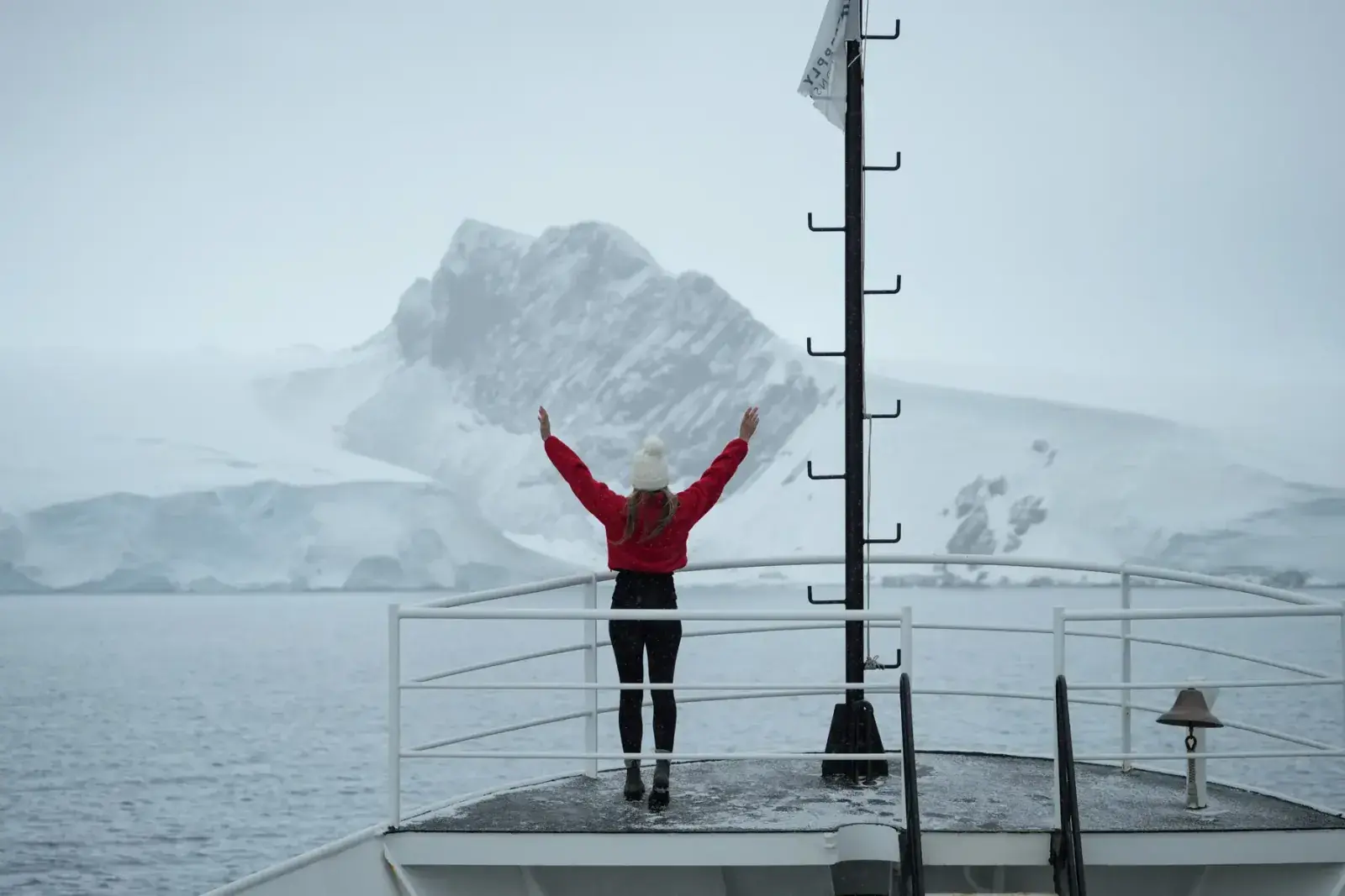 A woman holds her arms up on the bow of a ship in Antarctica