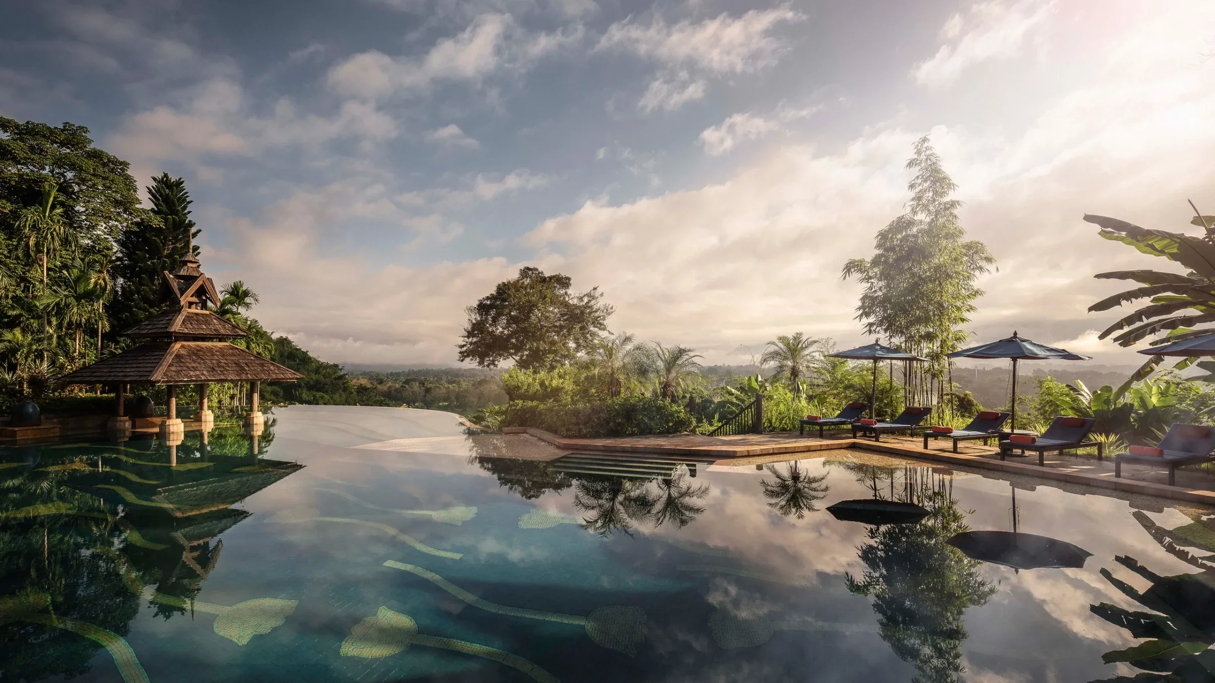 An infinity pool and Thai sala pavilion overlooking jungle hills at sunrise