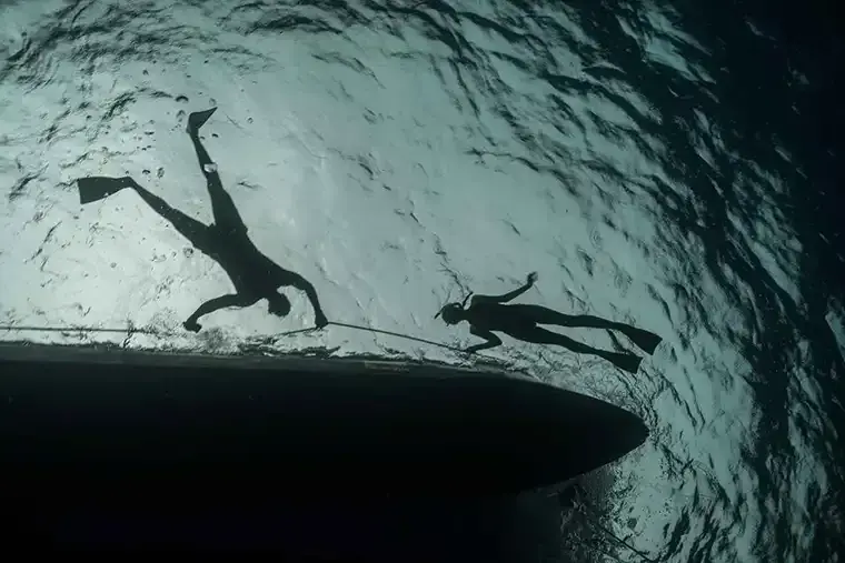 Upward shot of two swimmers hanging onto a boat